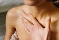 A person wrapped in a towel gently rubs traces of a cream coloured body lotion, into chest and around their collar bone.