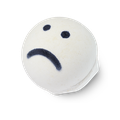 Sad Face, a white, circular-shaped bath bomb with two black dots for eyes and a black frown line.