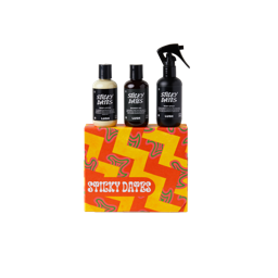 Sticky Dates. A square gift box wrapped in orange and yellow zigzag patterned paper. Three LUSH products are sitting on top of the box including Sticky Dates body lotion, shower gel and body spray. 