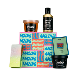 Amazing. A square gift box designed with a contrasting, block-colour pattern with the word "Amazing" printed repeatedly across. There are 4 Lush products sitting around the gift box and a limited edition pin badge which reads "Amazing". 