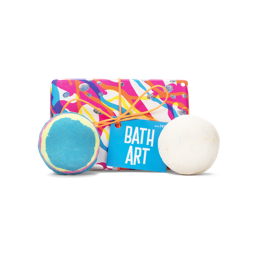 A gift in pink paper with white, blue and yellow swirls. Two bath bombs sit beside it - one white and one blue, pink and yellow.