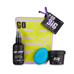 Go Big. A tall, fabric, pink and yellow zip pouch bag with three LUSH hair care products sat in front. There is a hair mist spray, a solid conditioner bar and a LUSH tub of shampoo. 