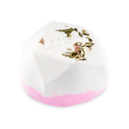 Hanami. A white, half bath bomb with a flat base in a geometric dome shape. The top is sprinkled with dried green botanical leaves and features embossed "LUSH" text, with a layer of pink at the base.