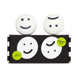 Happy Face bath bomb and Sad Face bath bomb sit on top of a black and white box with the same designs and green stickers.