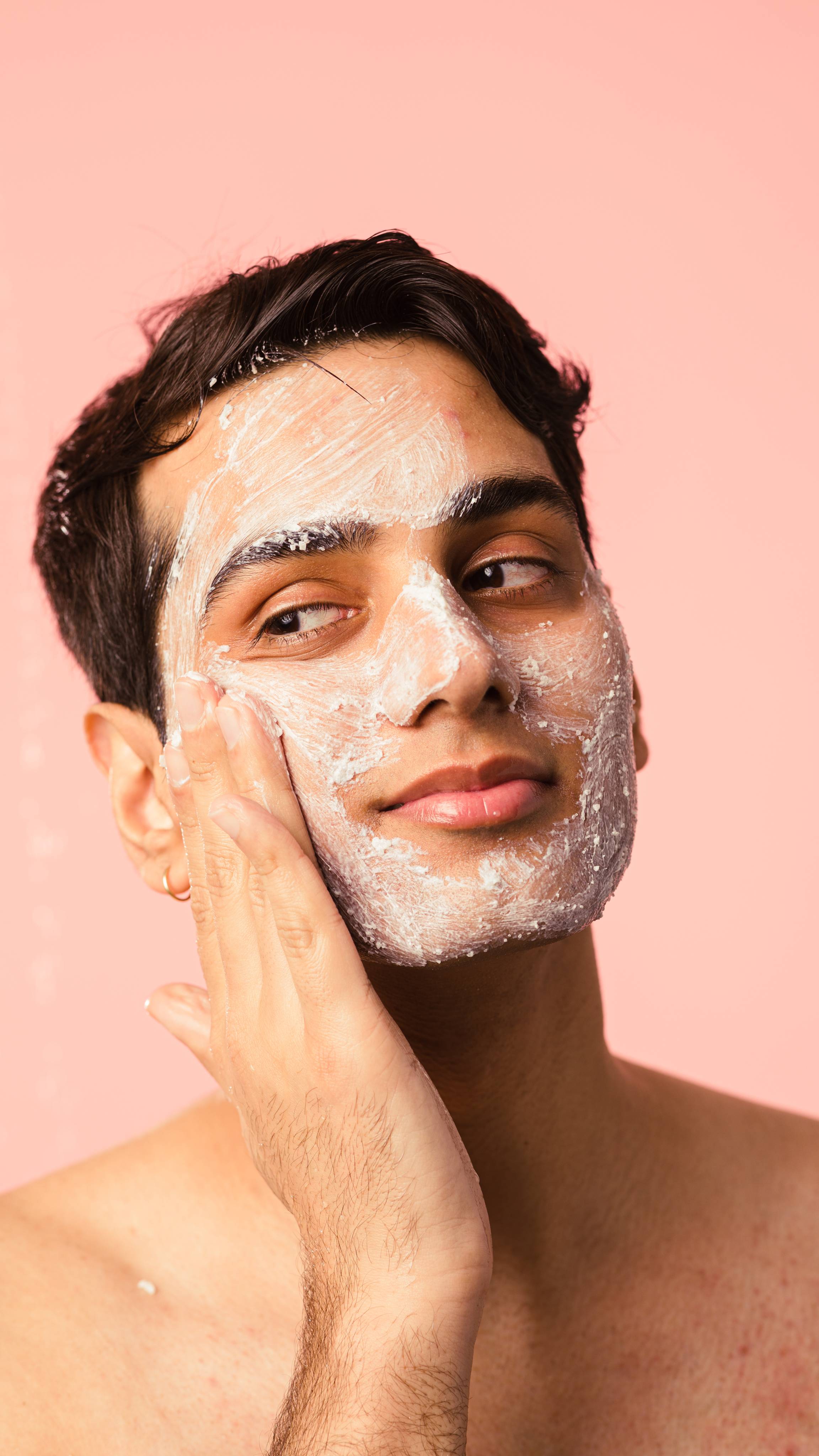 Model is applying the exfoliating Ocean Salt scrub gently onto their face on a light beige background.