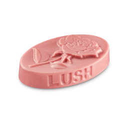 Rose Argan. An oval massage bar with a pinkish tint. A rose flower is embossed on the top with the word LUSH on the side.