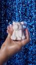 A close-up of the model holding the Snow Bear soap upright with one hand under shower water. 