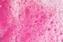 Image shows a close of of the bright, bubblegum-pink bath water surrounded by a blanket of bubbles.
