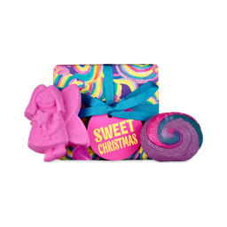 Sweet Christmas. A brightly-coloured, wrapped gift box with lots of pink, purple and blue swirls, tied with a teal ribbon and pink tag. There are two bath products that stand against the box. There is a pink fairy bath bomb and a swirled bubble bar. 