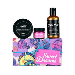 Sweet Dreams. A short, rectangular gift box wrapped in purple paper decorated with illustrations of crescent moons and hot air balloons. There are Three Lush products sitting on top of the box; including a body lotion, shower gel and lip mask. 