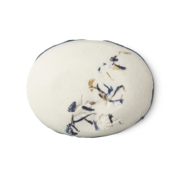T'eo. A white, oval shaped solid deodorant block. It is smooth and powdery, with dried Cornflower petals and a blue wax edging.