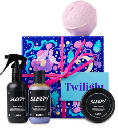 Twilight. A square gift box with blue, purple and pink butterfly and sleeping caterpillar designs, wrapped in a pink ribbon. There are four LUSH products surrounding the box including a bath bomb, shower gel, body spray and body lotion.