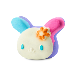 U.SA.HA.NA. A colourful bath bomb shaped like a bunny character's head with a cream face, blue eyes, and an orange flower. One ear is bright blue and the other is pink, with purple accents throughout.